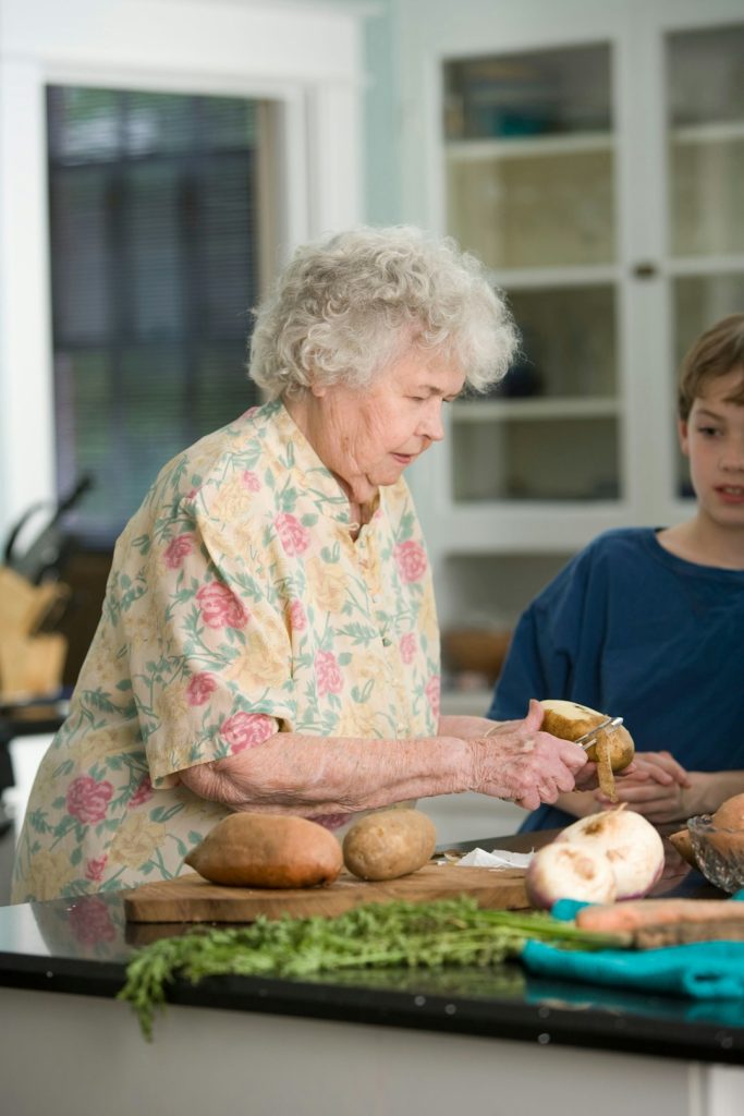 Crafting Captivating Headlines: Your awesome post title goes here Properly preparing fresh, uncooked produce is a must, and with this in mind, the elderly woman pictured here was teaching her grandson how to do just that, while peeling a number of potatoes.
She was imparting her knowledge of how to safely use a knife to accomplish the peeling. During such activities, when using sharp instruments, injury prevention need be foremost in one’s mind.